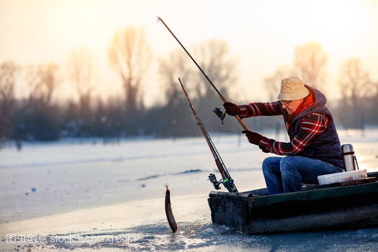 愉快的渔夫在结冰的河捉住鱼在冬天