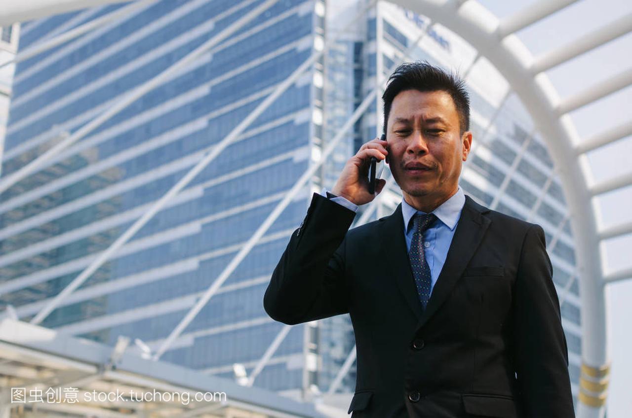 中年亚裔商人穿着现代黑西装打电话与移动智能
