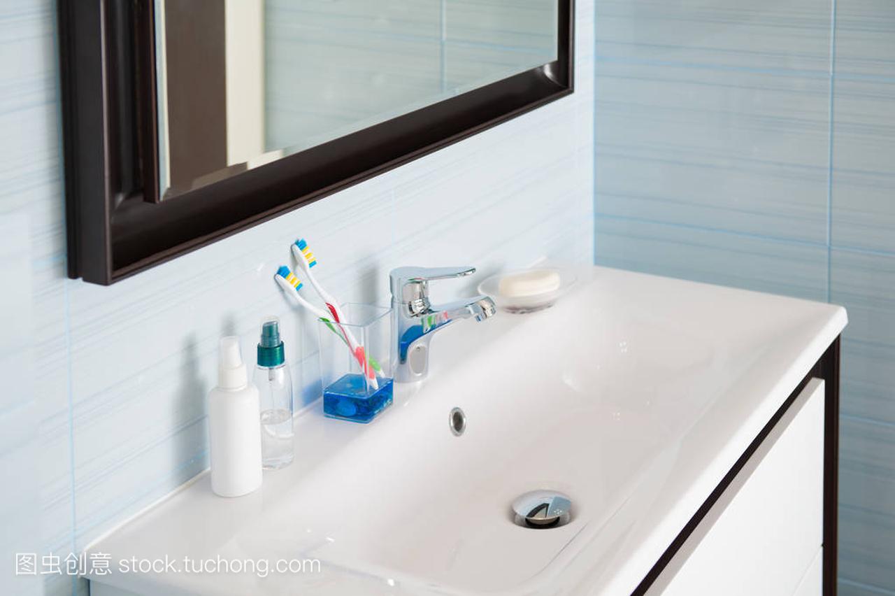 明亮的蓝色白色卫生间与洗涤盆用牙刷和铬搅拌