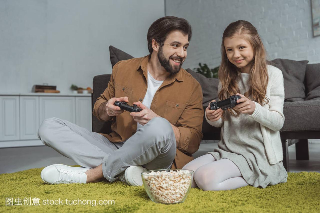 父亲和女儿坐在地毯上玩电子游戏