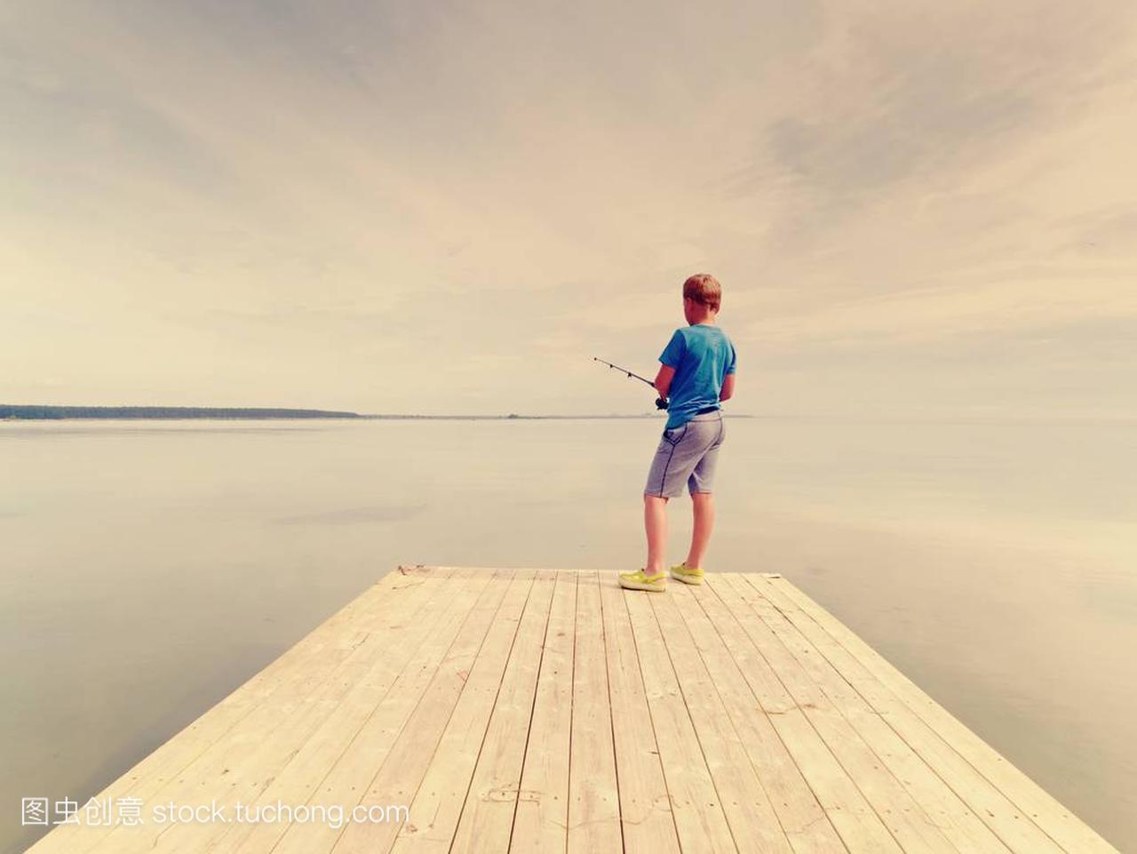 夏天的时候, 小男孩在木痣上钓鱼。蓝色 t-shirt