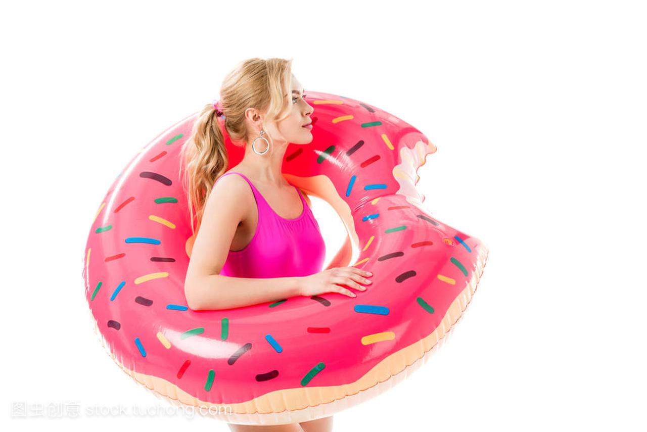 金发女郎在粉红色的泳装举行甜甜圈游泳戒指被