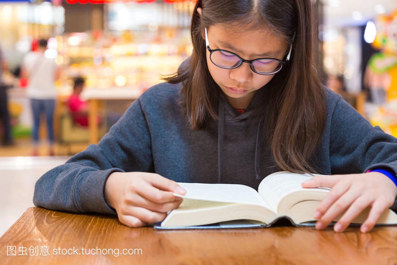 戴眼镜的女孩在桌子上看厚小说故事书
