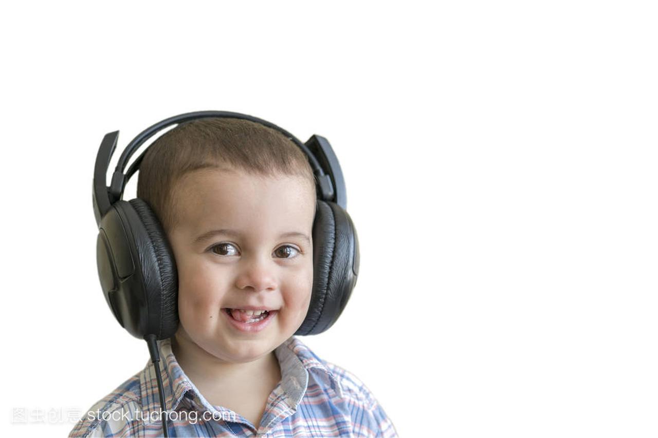漂亮的小男孩戴着大耳机。穿着格子衬衣听音乐