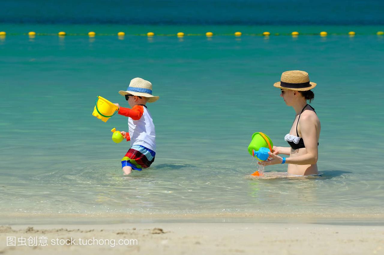 两岁的小男孩玩沙滩玩具与母亲在海滩上