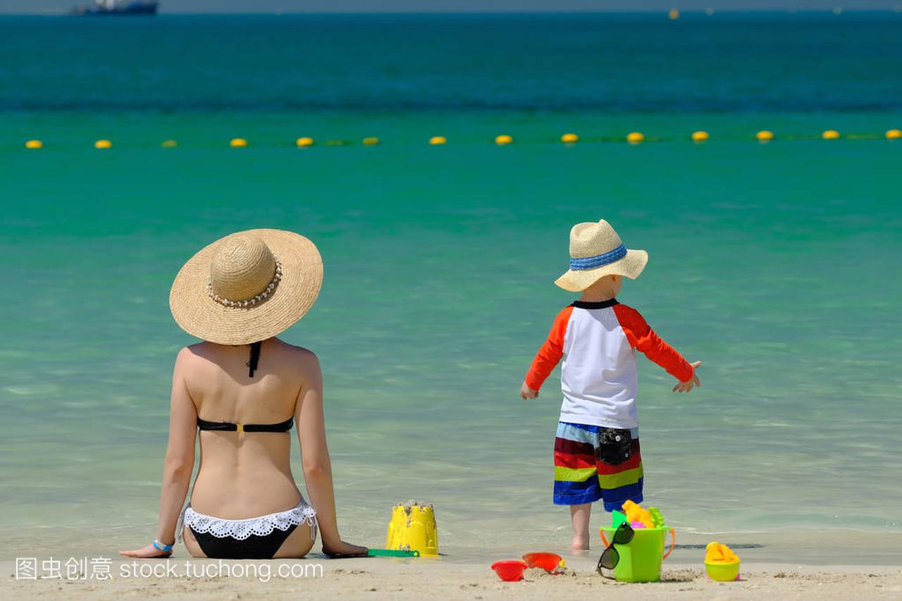 两岁的小男孩玩沙滩玩具与母亲在海滩上