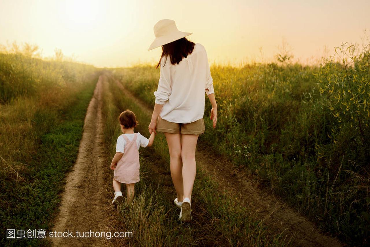 一个漂亮的母亲在帽子和小漂亮的女儿走在田野