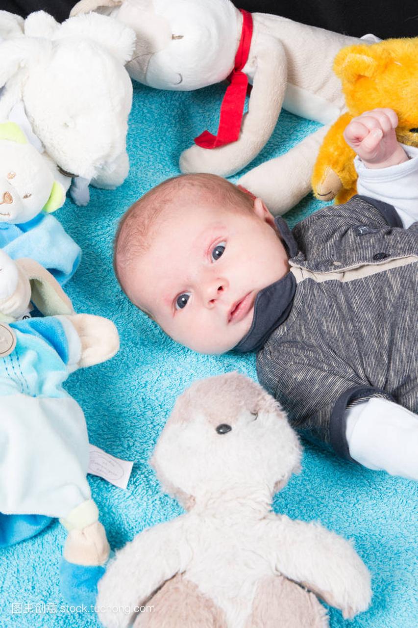 婴儿男孩与他柔软的玩具长毛绒躺在柔软的蓝色