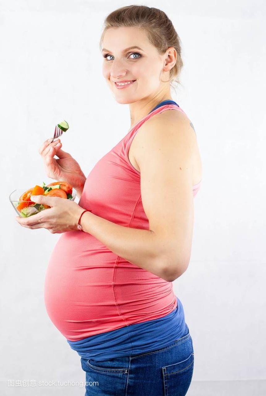 年轻漂亮的孕妇正在吃蔬菜沙拉。那个女孩拿着