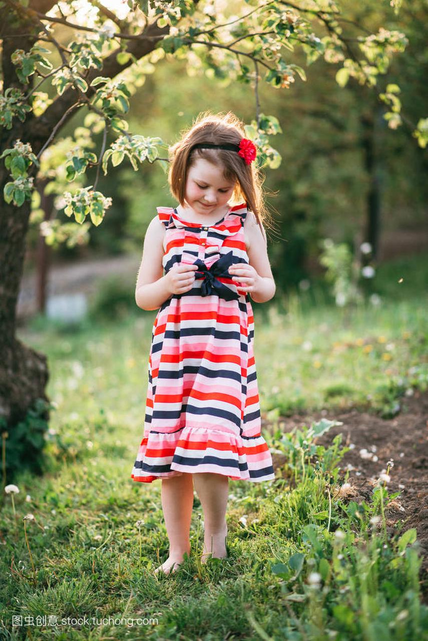 小可爱的女孩装订弓安城礼服在盛开的花园