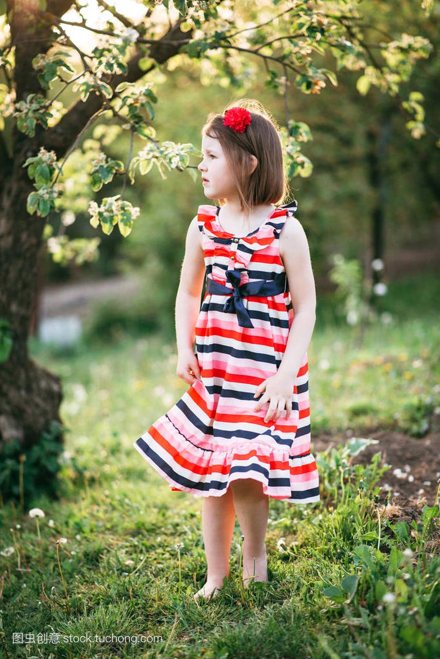 小可爱的女孩在礼服和头带走在盛开的花园