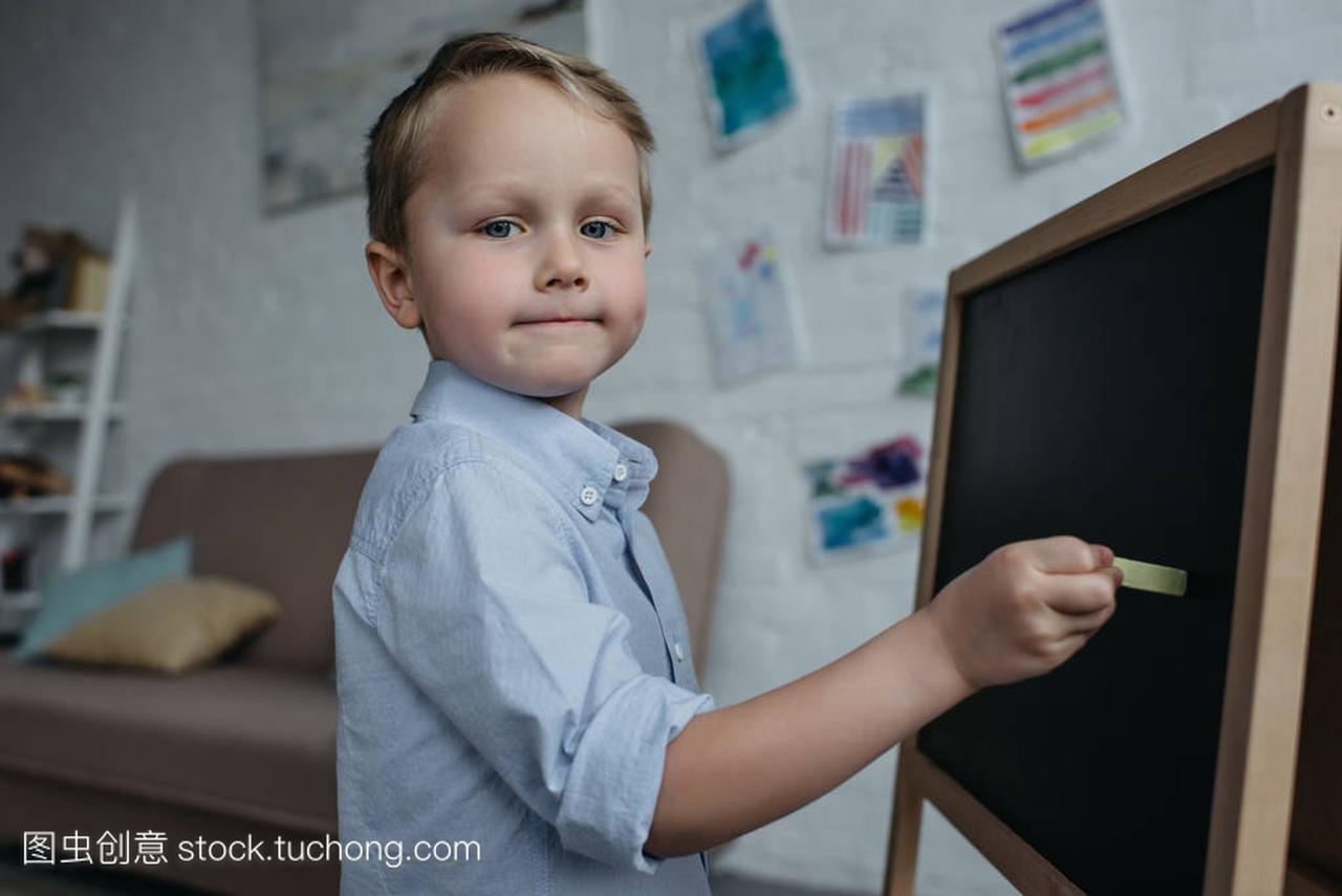 小男孩的侧面看着粉笔在黑板上画画的时候在家