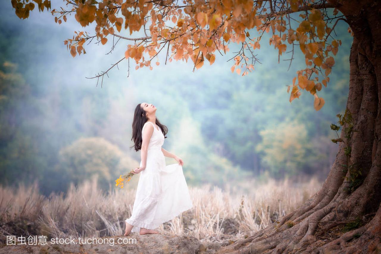 穿着白色连衣裙的年轻漂亮女子享受自然之树