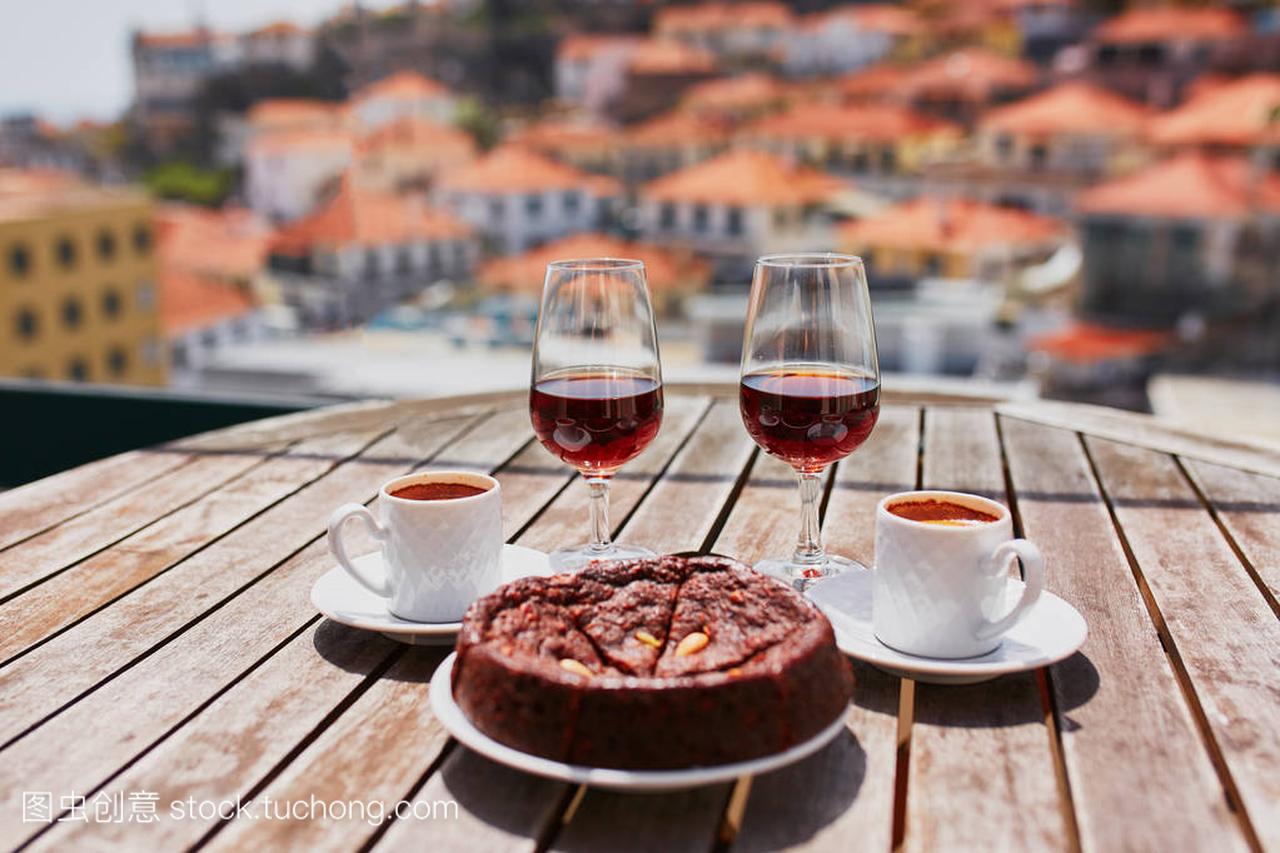 马德拉岛两杯酒，两杯新鲜咖啡和传统葡萄牙蜂蜜坚果甜点博洛德梅尔在咖啡馆与葡萄牙马德拉丰沙尔进城的视图