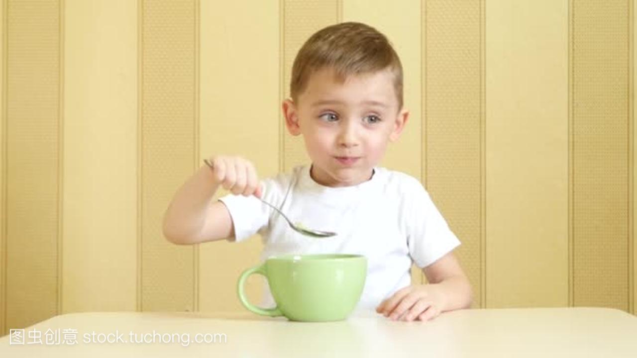 一个快乐的孩子坐在餐桌边吃着一勺盘子里的汤