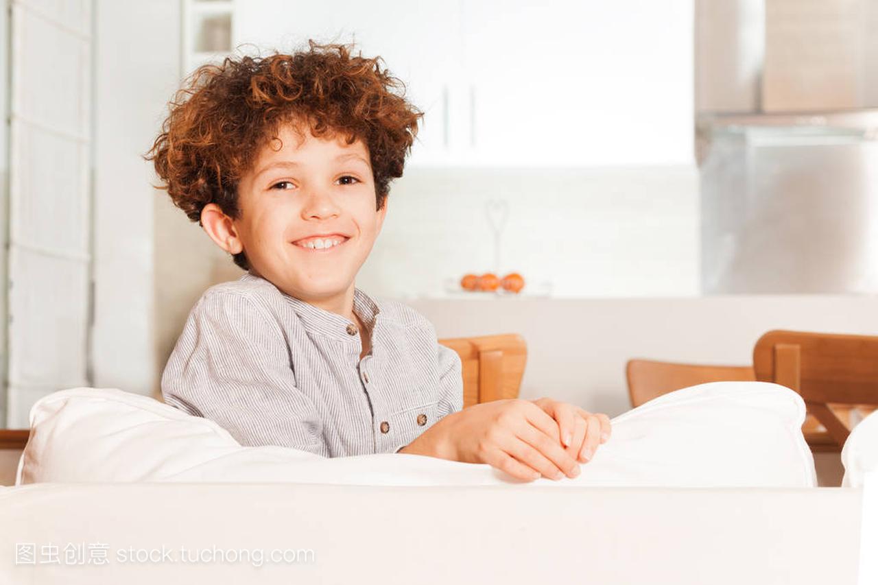 青春期卷曲头发的男孩坐在白色沙发在休息室里