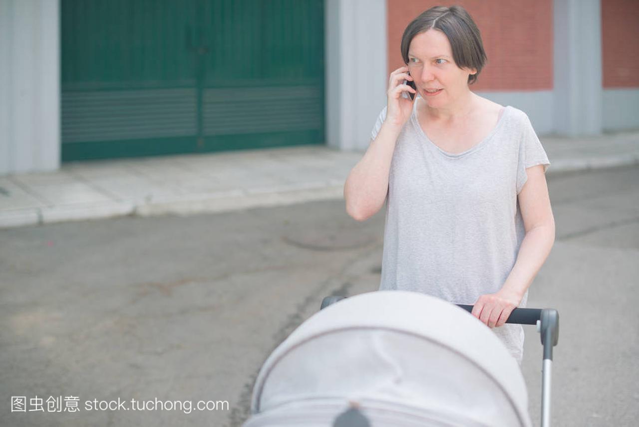 不安和担心的母亲谈论手机和推婴儿在推车, 而
