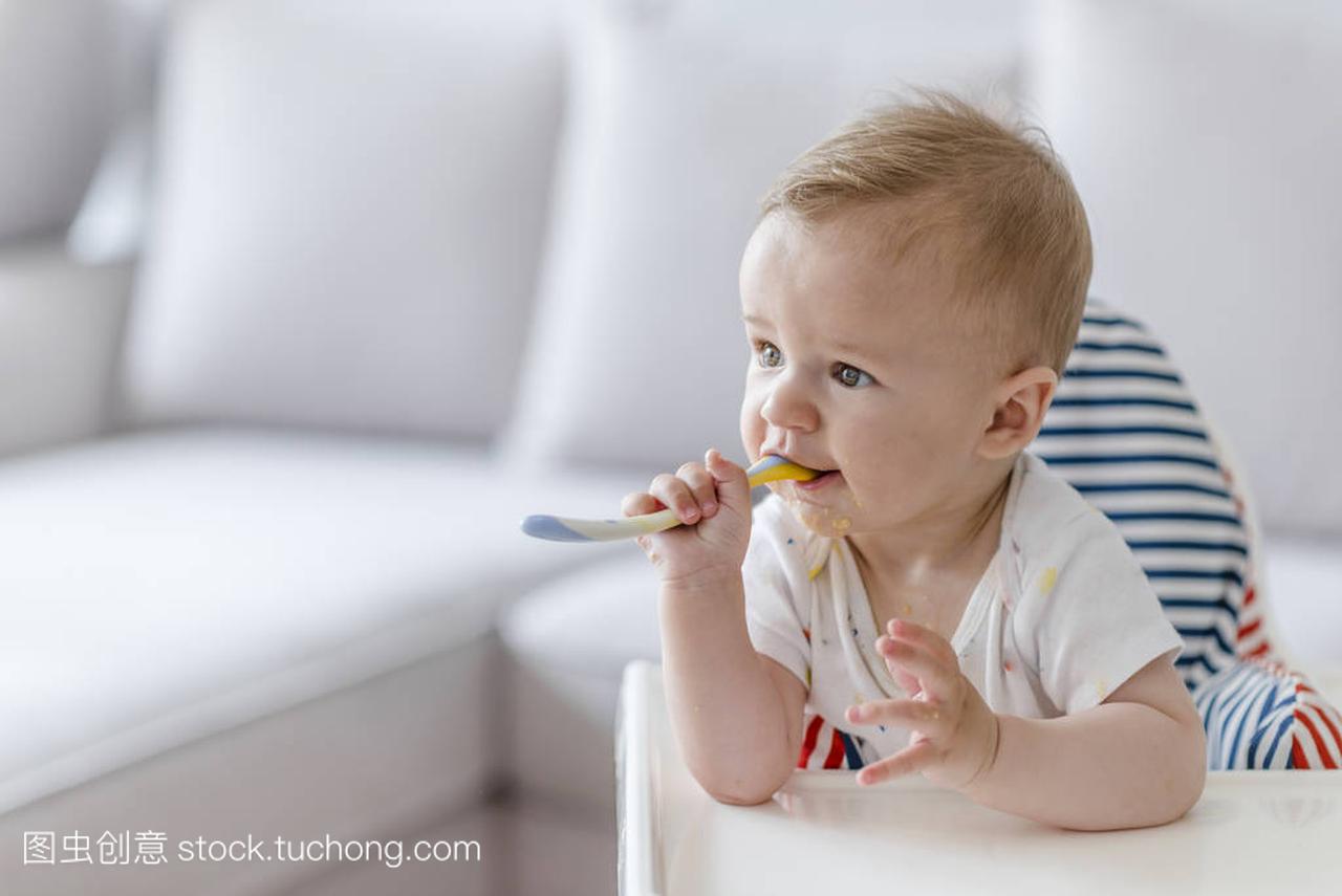 快乐的婴儿用勺子吃食物。快乐的婴儿吃自己。