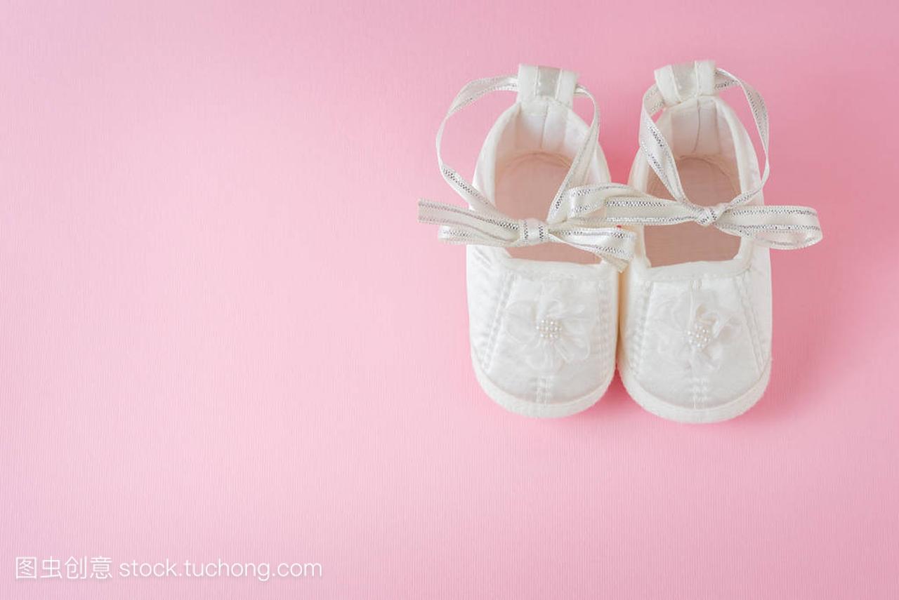 粉红色背景的白色婴儿鞋。一双婴儿鞋。是个女