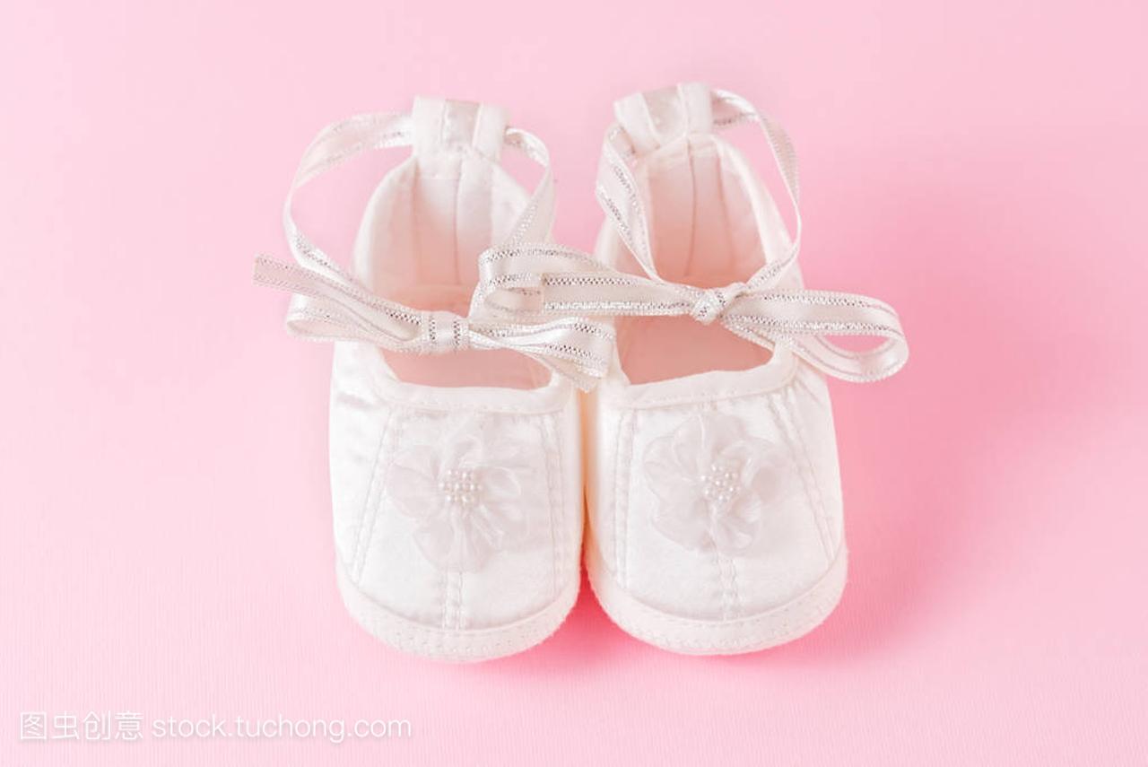 粉红色背景的白色婴儿鞋。一双婴儿鞋。是个女