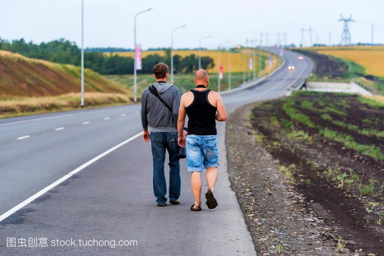 Two men walk along asphalt road back view