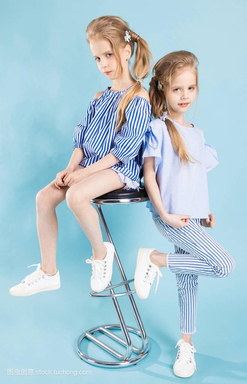 穿浅蓝色衣服的女孩双胞胎在蓝色背景的酒吧凳