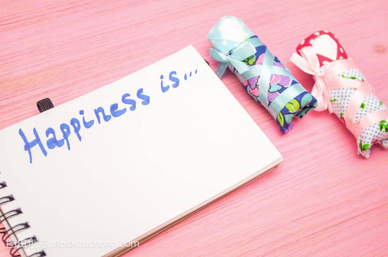 Happiness is inscription in notepad and baby diapers on purple wooden board background.