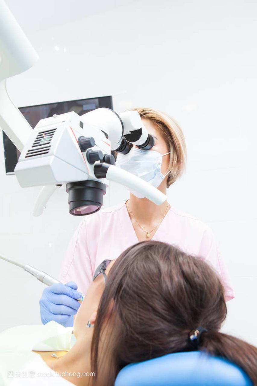 年轻的女牙医治疗根管显微镜在牙科诊所。年轻