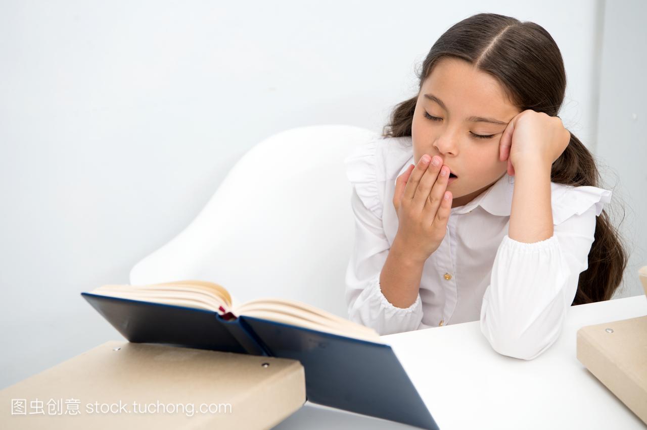 Boring literature. Girl child reads book while sit table white background. Schoolgirl studying and reading book. Kid girl school uniform bored yawning face sadly read boring literature. Tiresome task.