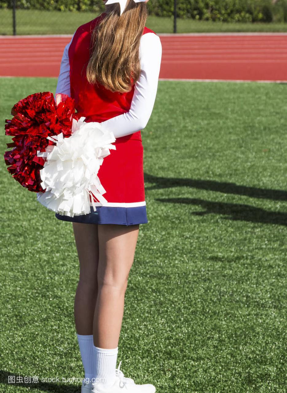 her pom poms behind her on a turf field.