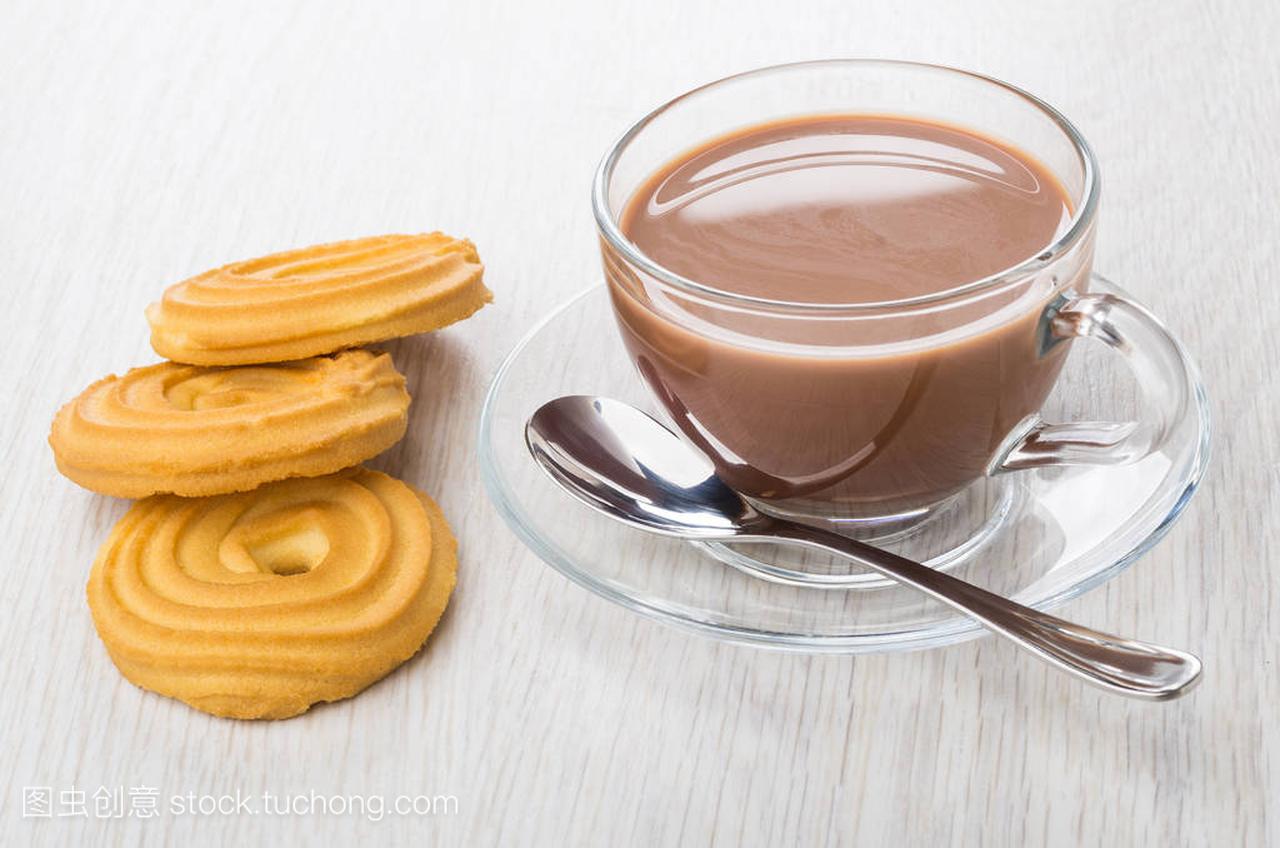 Cocoa with milk in cup, spoon on saucer, cookies on wooden table