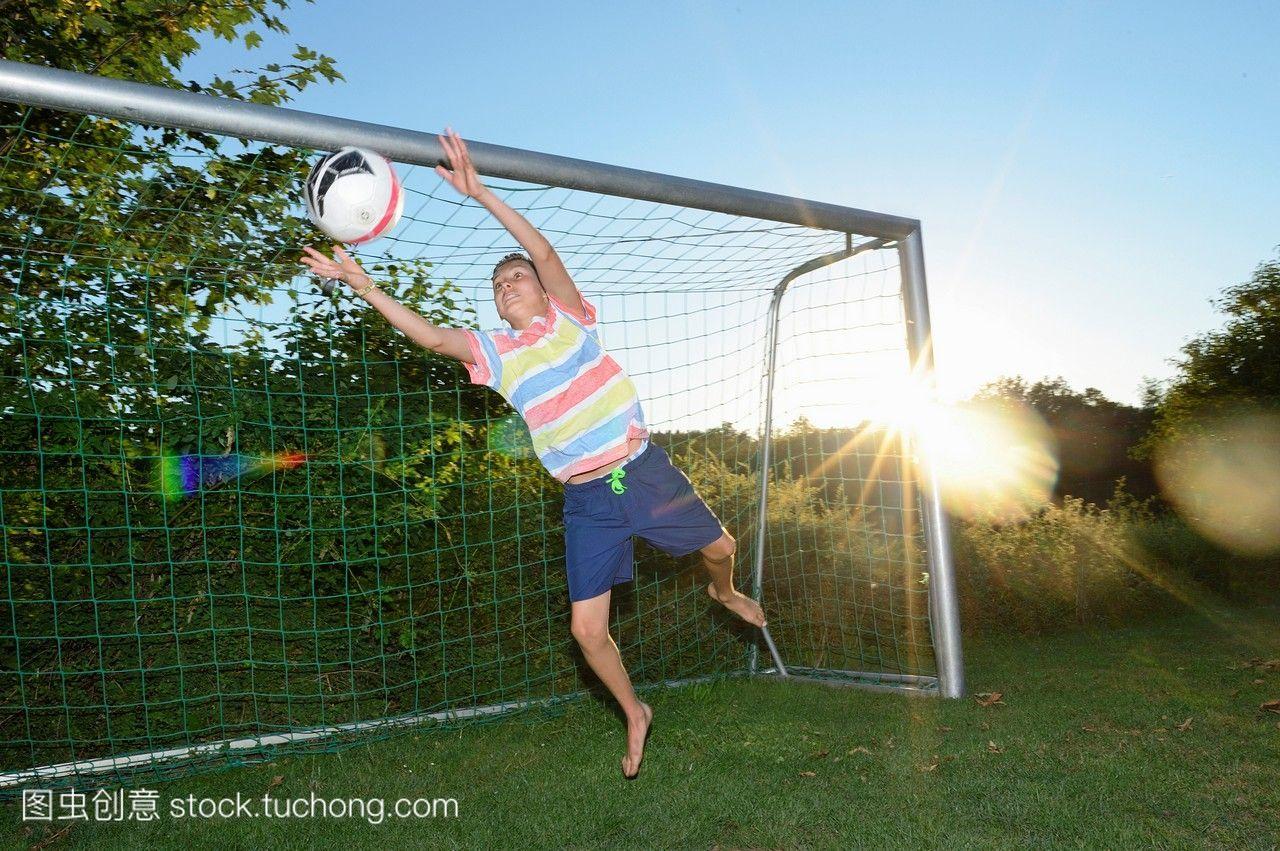 年轻的男孩当守门员在草地上踢足球,德国。