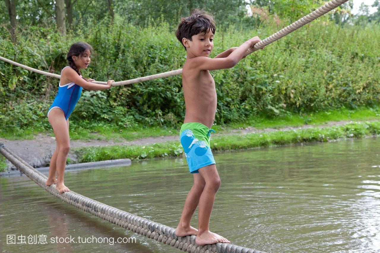 穿游泳衣的孩子在水上的绳子上保持平衡。