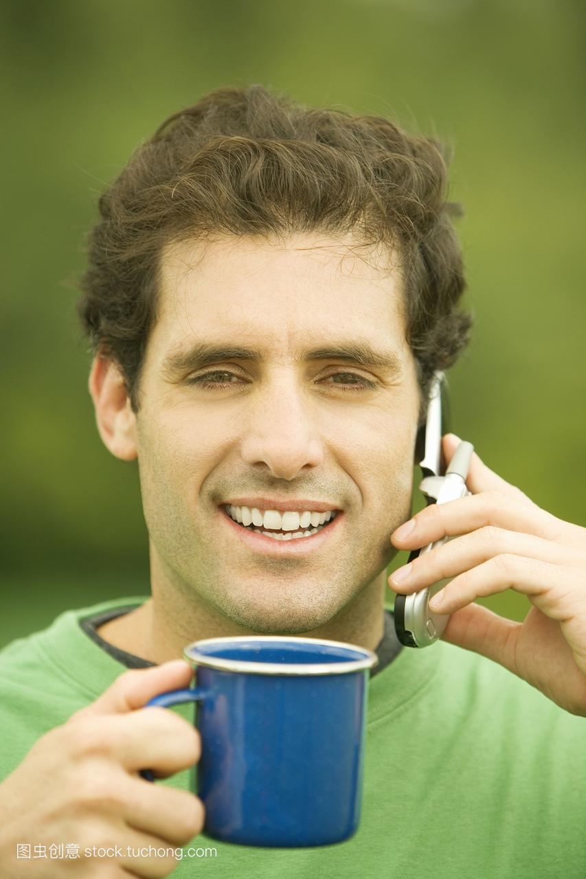 一名中年男子用手机端着一杯咖啡的画面