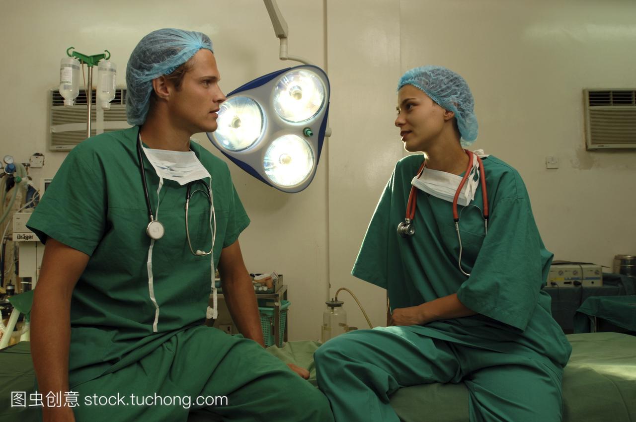 一个男医生和女护士在绿色手术长袍和帽子坐在