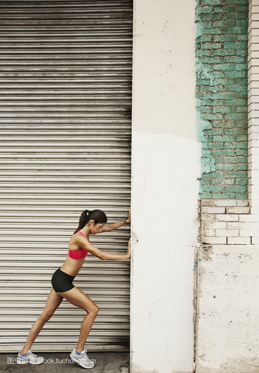一个女人在跑步装备背心和短裤伸展自己的身体