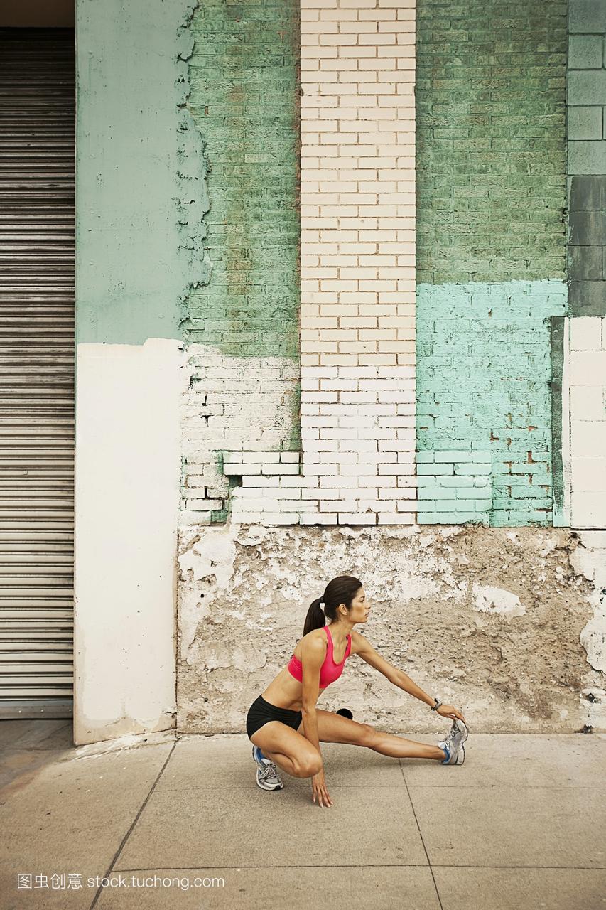 一个女人在跑步装备背心和短裤伸展自己的身体