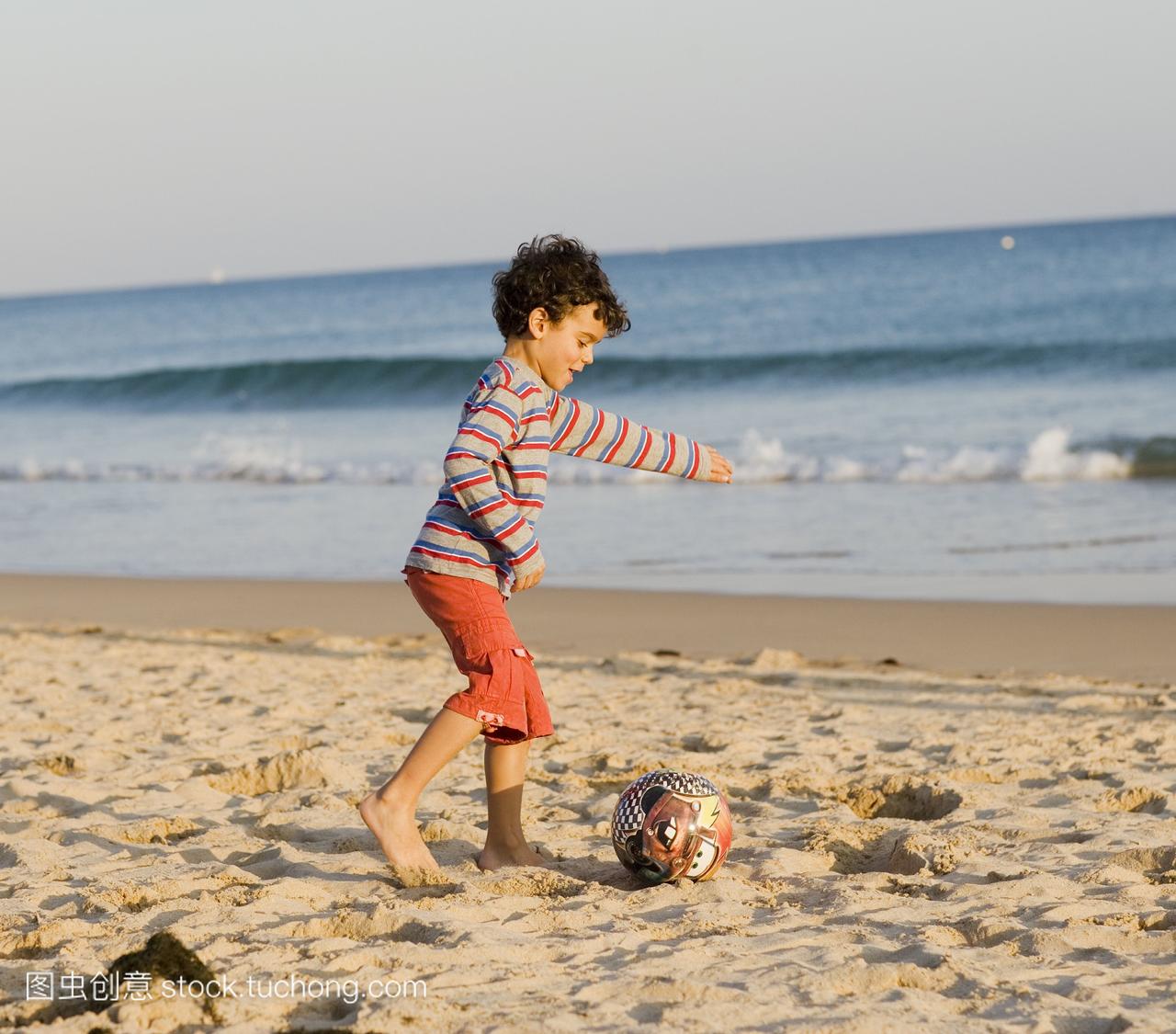 一个男孩在沙滩上玩球,葡萄牙。