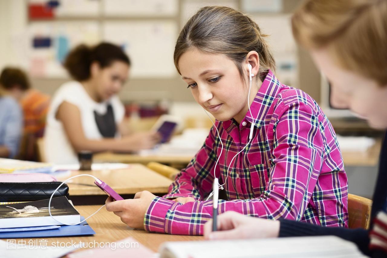 在教室里,女学生通过智能手机听音乐