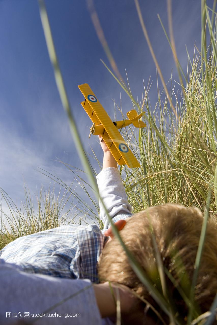 男孩7-9岁抱着玩具飞机,躺在长草上,低角度看