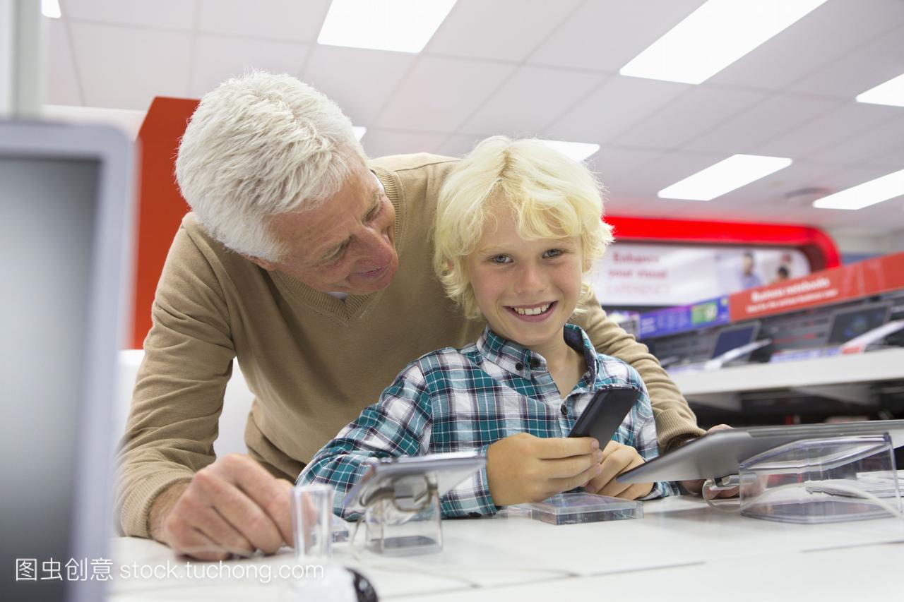 在电子商店里,微笑的孙子看着手机和祖父的照片