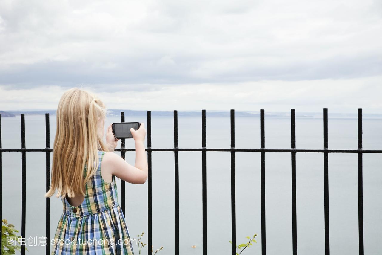 一个穿着格子背心的女孩拿着智能手机拍照。
