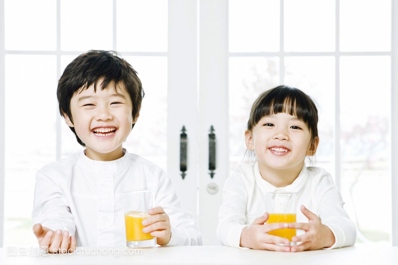 男孩和女孩坐在桌子上,喝着橙汁