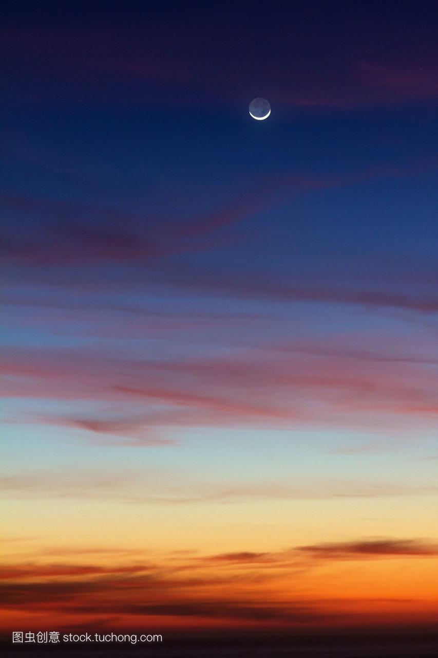 一弯新月在美丽的蓝色,紫色和橙色的天空中日