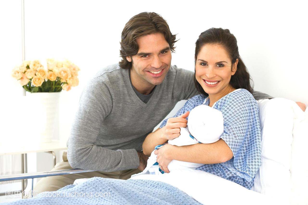 西班牙夫妇抱着刚出生的婴儿躺在医院的病床上