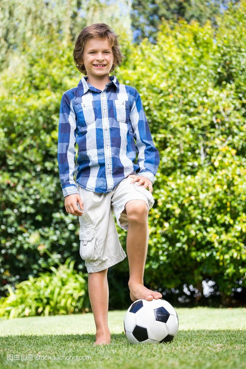 一个可爱的男孩在公园的足球上微笑着,用脚摆