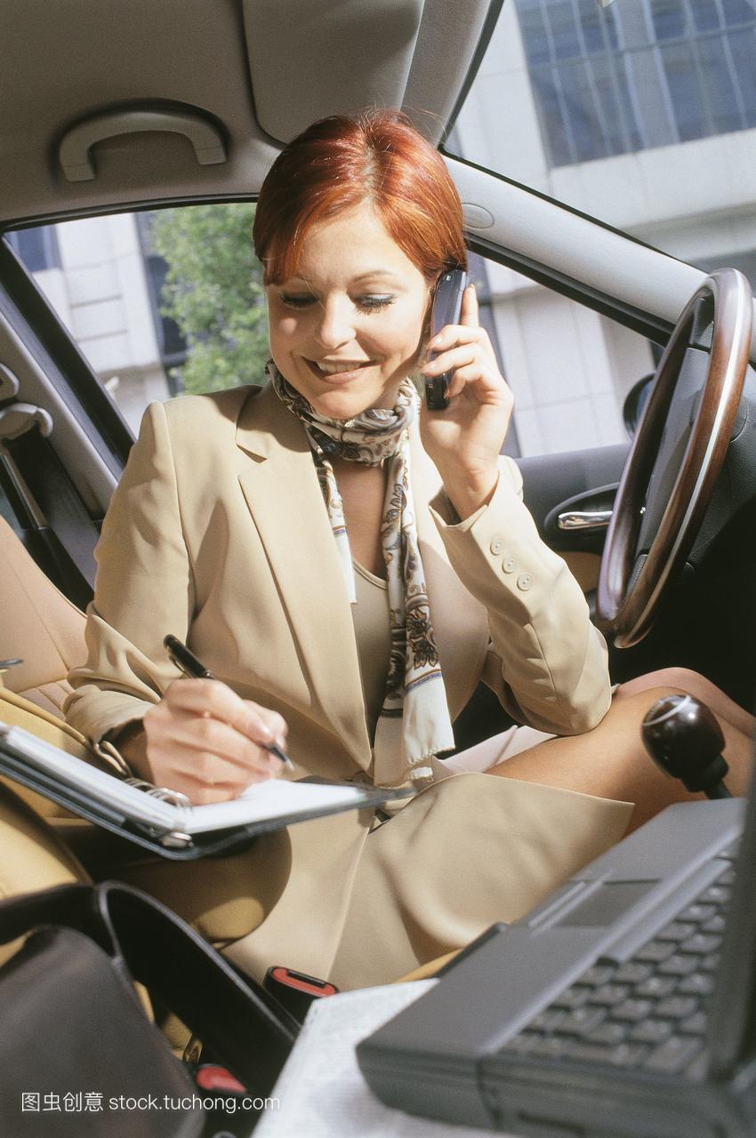 微笑的女商人在车里,在电话上,记日记,包和电脑