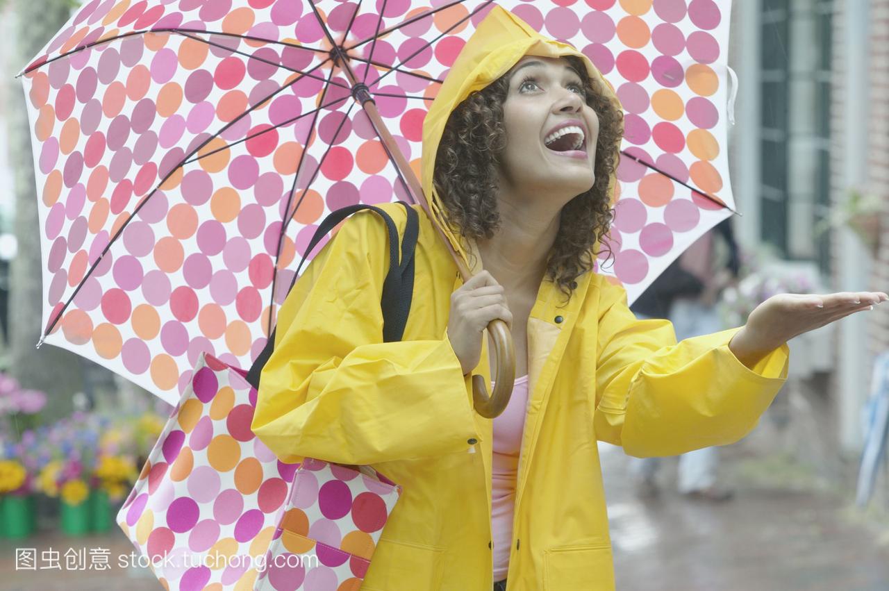 穿着雨衣的西班牙裔妇女带着雨伞检查下雨