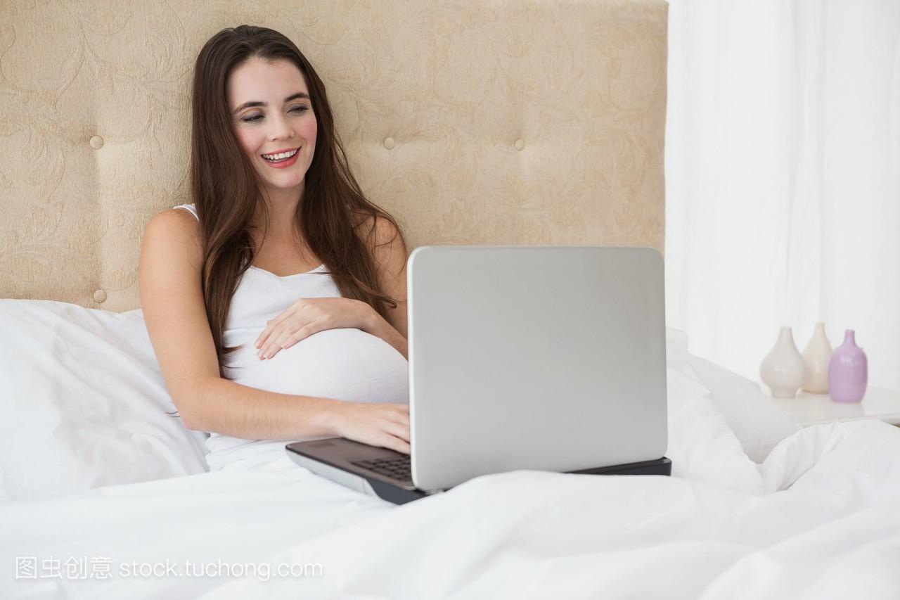 在床上用笔记本电脑怀孕的黑发女郎