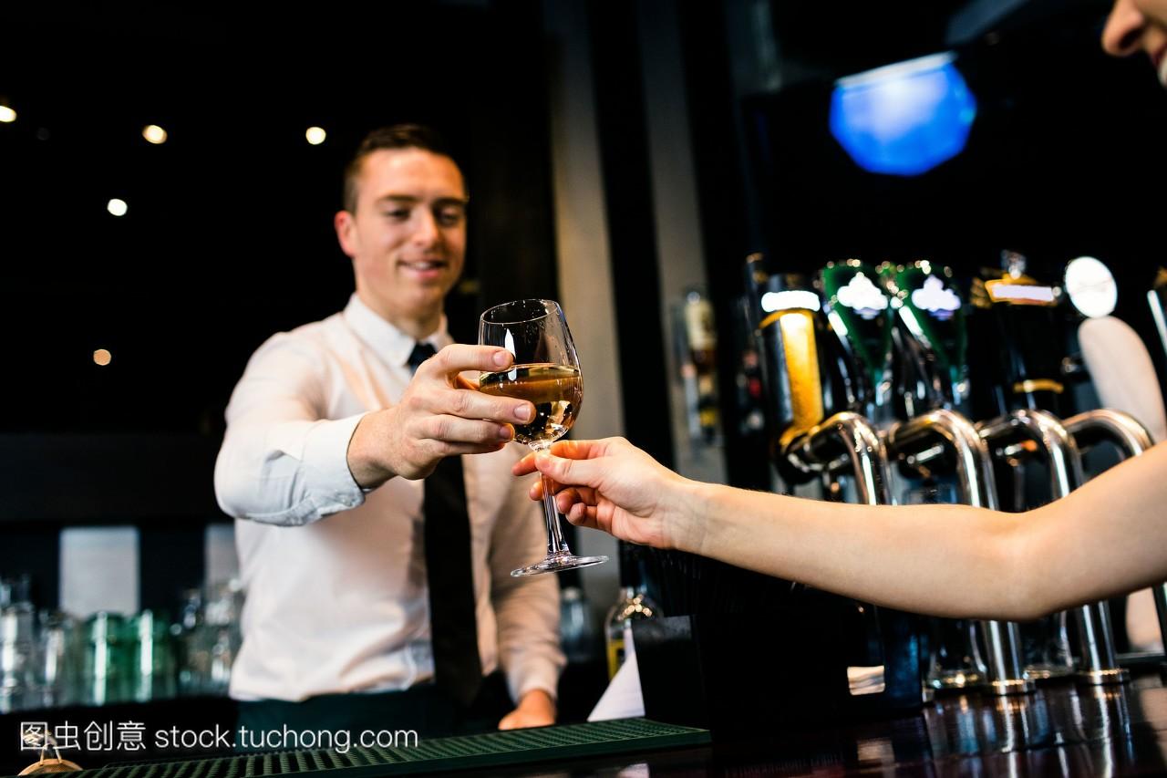 一个微笑的酒吧侍者给客户端上一杯白葡萄酒